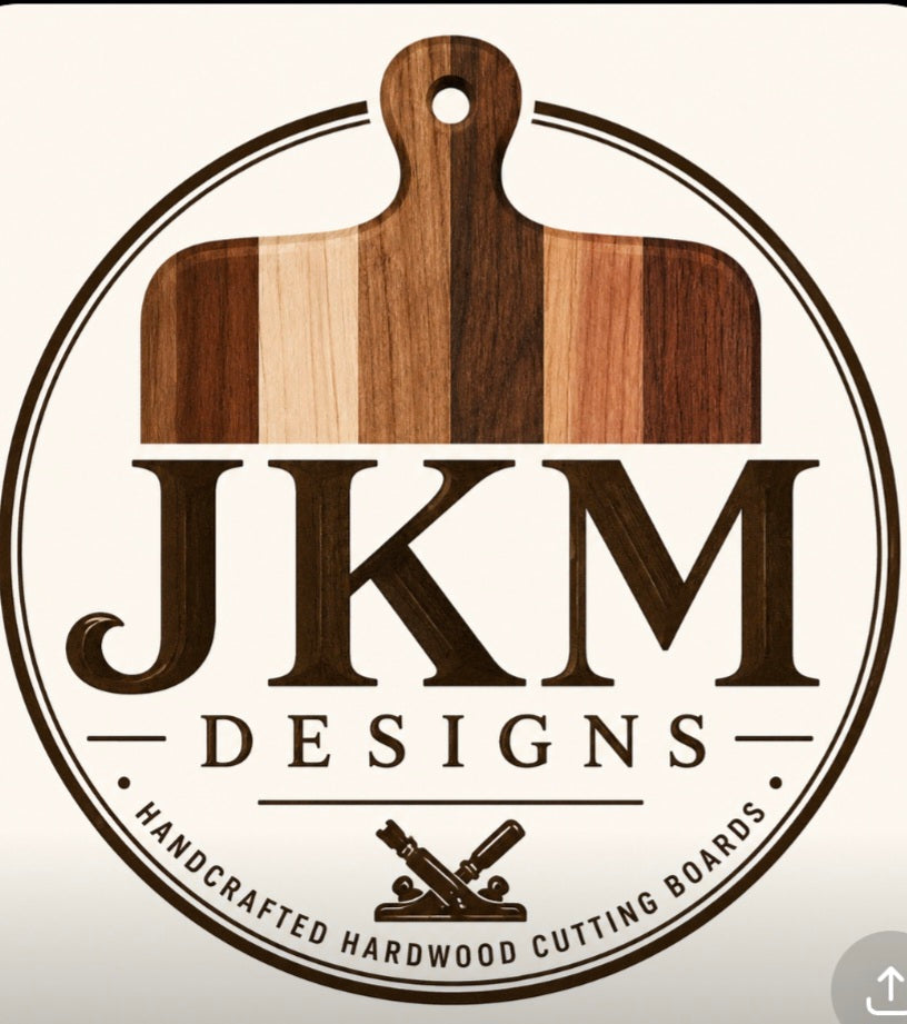 A circular logo for JKM Designs featuring a striped wooden cutting board motif above the text 'JKM DESIGNS' and the phrase 'Handcrafted Hardwood Cutting Boards' on a light cream background.